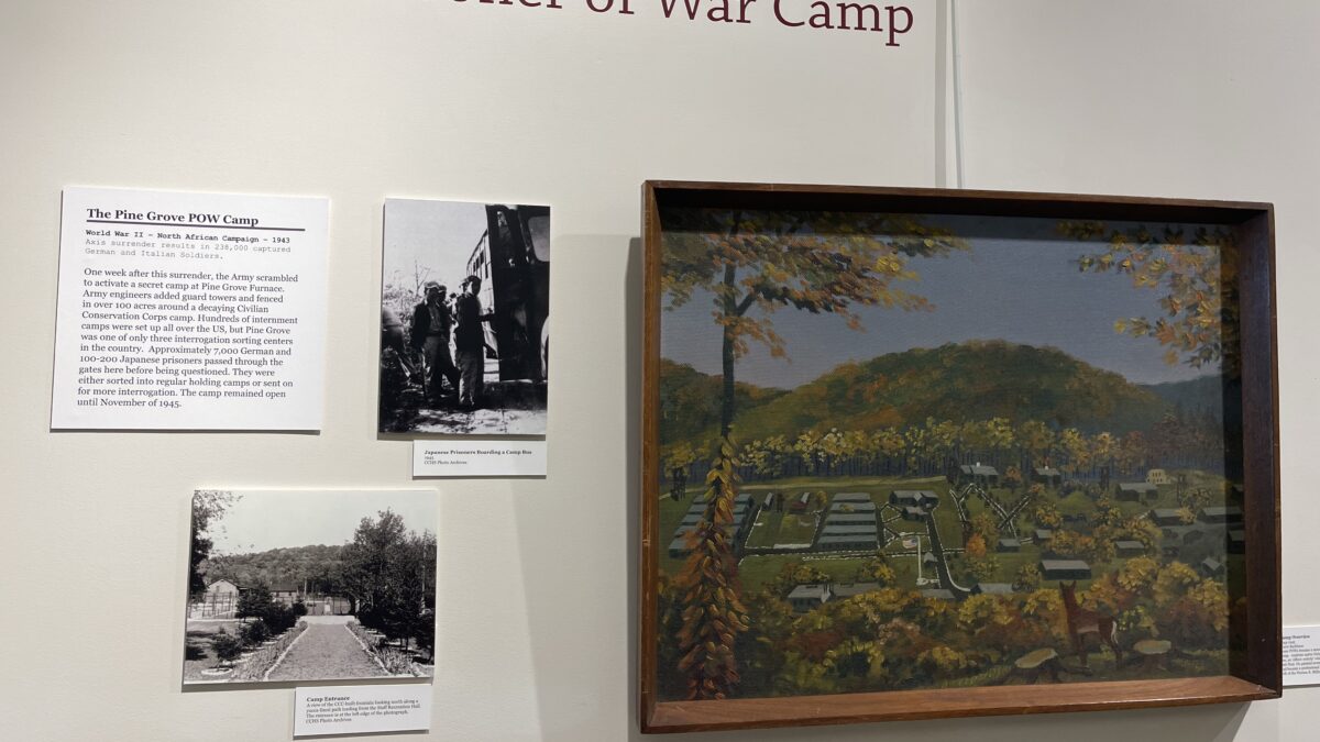A painting of the Pine Grove Prisoner of War Camp hangs in an art gallery, part of an art exhibition in a museum room.