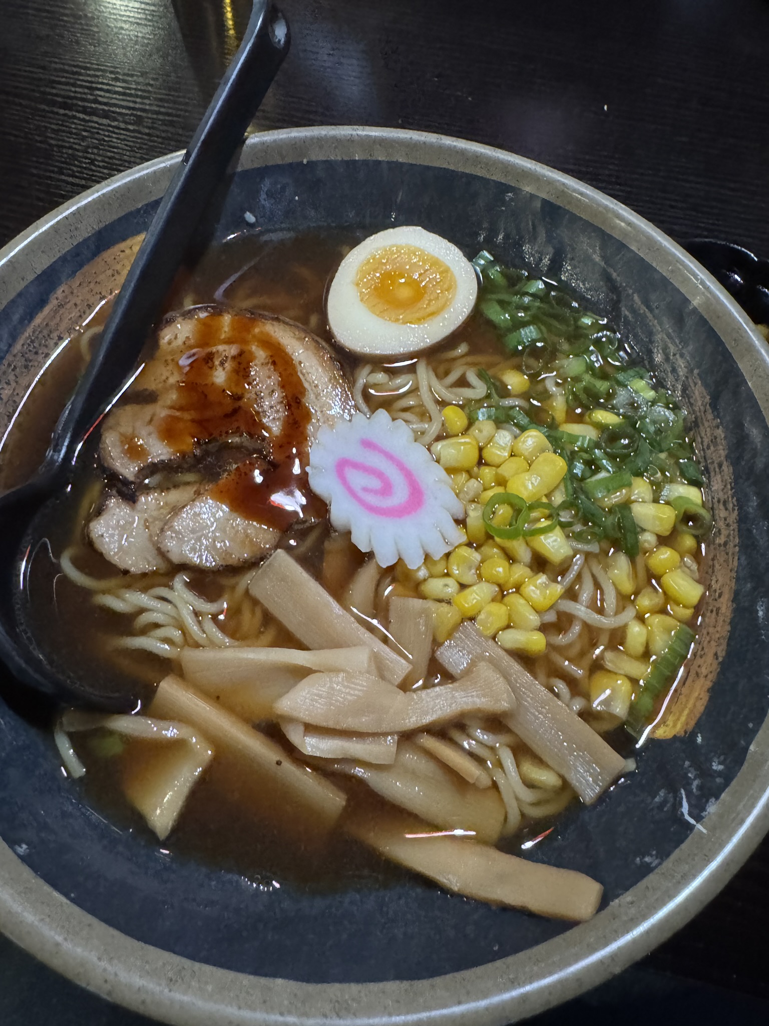 ramen soup with a fish cake and egg on top. corn, green onions, beef, and bamboo shoots can be seen. 