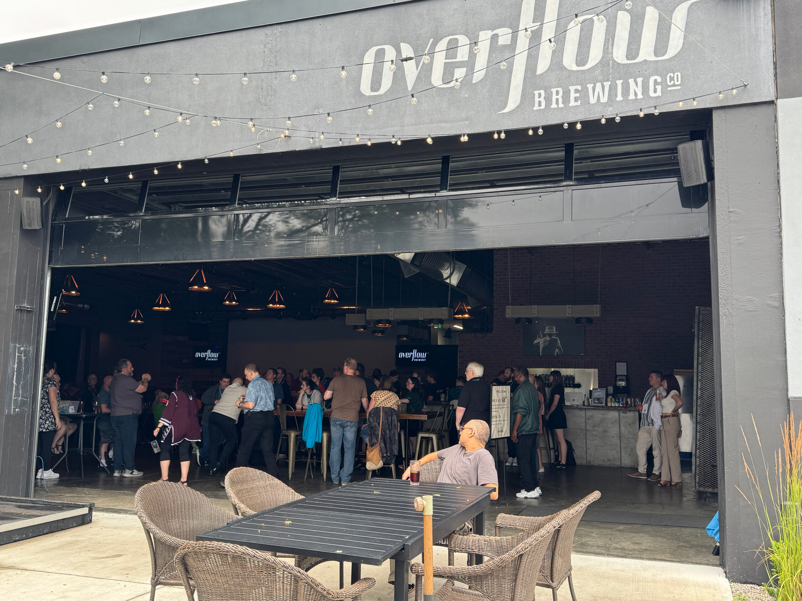 Overflow bar from the outside view. Patio tables appear before an open bay door to the brewery.  