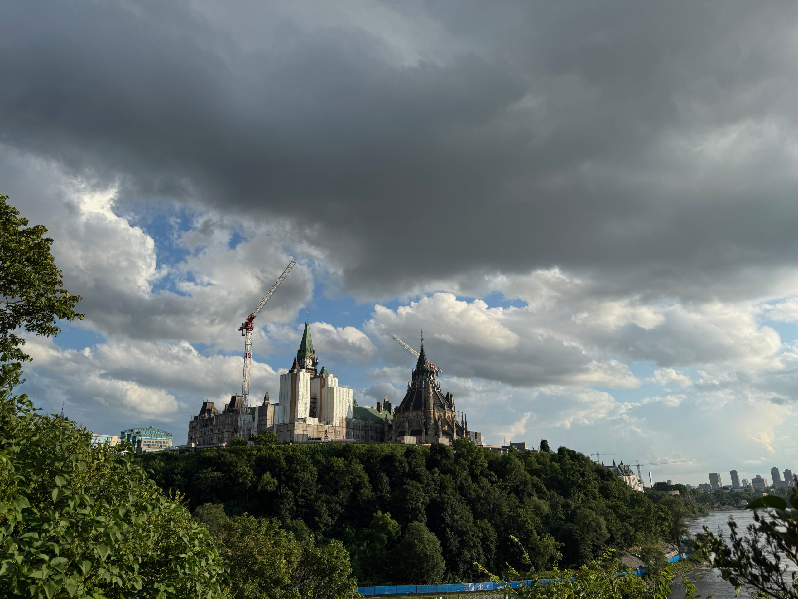 Looking at Parliament in Ottawa. The view shows breathtaking clouds and sky while Parlament sits atop a hill overlooking the river. 