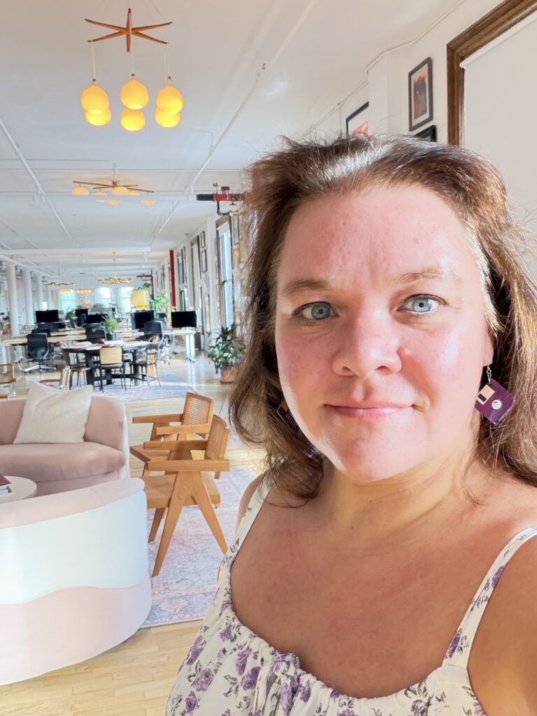 Courtney Robertson, wearing purple floppy disk earrings, takes a selfie inside Automattic’s sunlit NoHo office