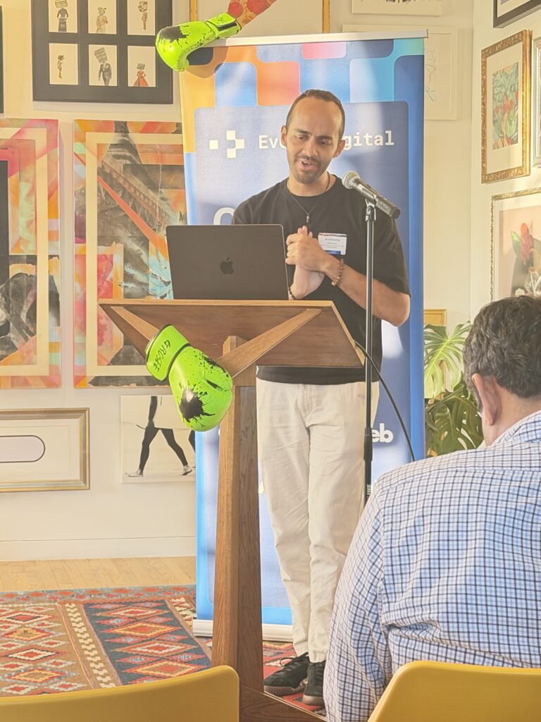 Anthony Bradshaw of Evolving Web speaks at a podium beside an EvolveDigital banner draped with neon green boxing gloves